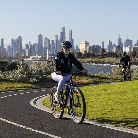 The city skyline is seen as people ride their bikes along a pathway in St Kilda, Melbourne.
