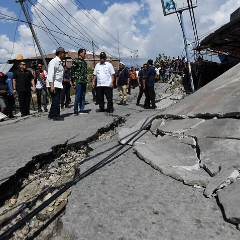 A handout photo made available by the Indonesian Presidential Palace showing Indonesian President Joko Widodo (C) looking at a ruined house