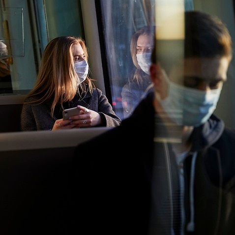 young woman sitting in train wearing protective mask, using smartphone