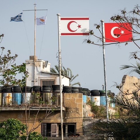Greek and Cypriot Republic flags in the background. Turkish and Turkish Cypriot flags acoss Cyprus' UN buffer zone