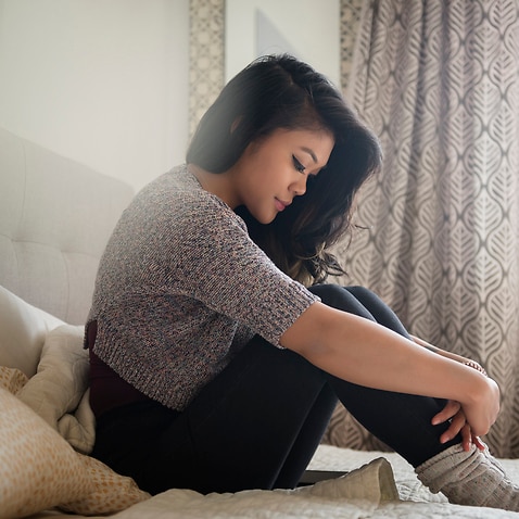 Depressed Mixed Race woman sitting on bed