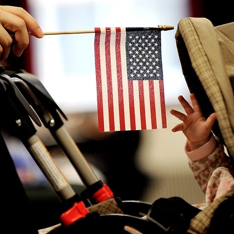 File: A baby reaches for an American flag held by her mother during naturalization ceremony at a federal building in New York