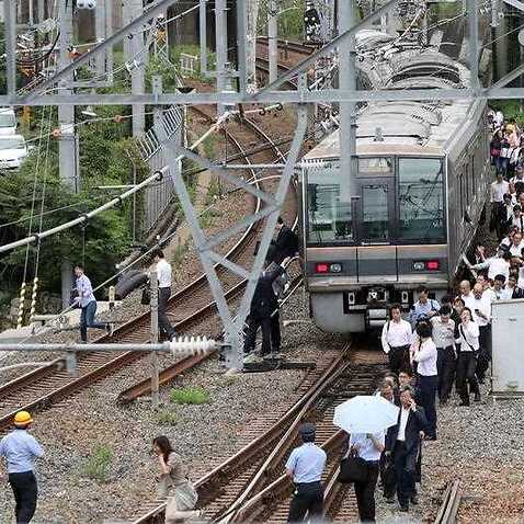 Passengers on board a commuter train walk on the railway due to suspended service, after a magnitude 6.1 earthquake hit western Japan, in Osaka, 18 June 2018.