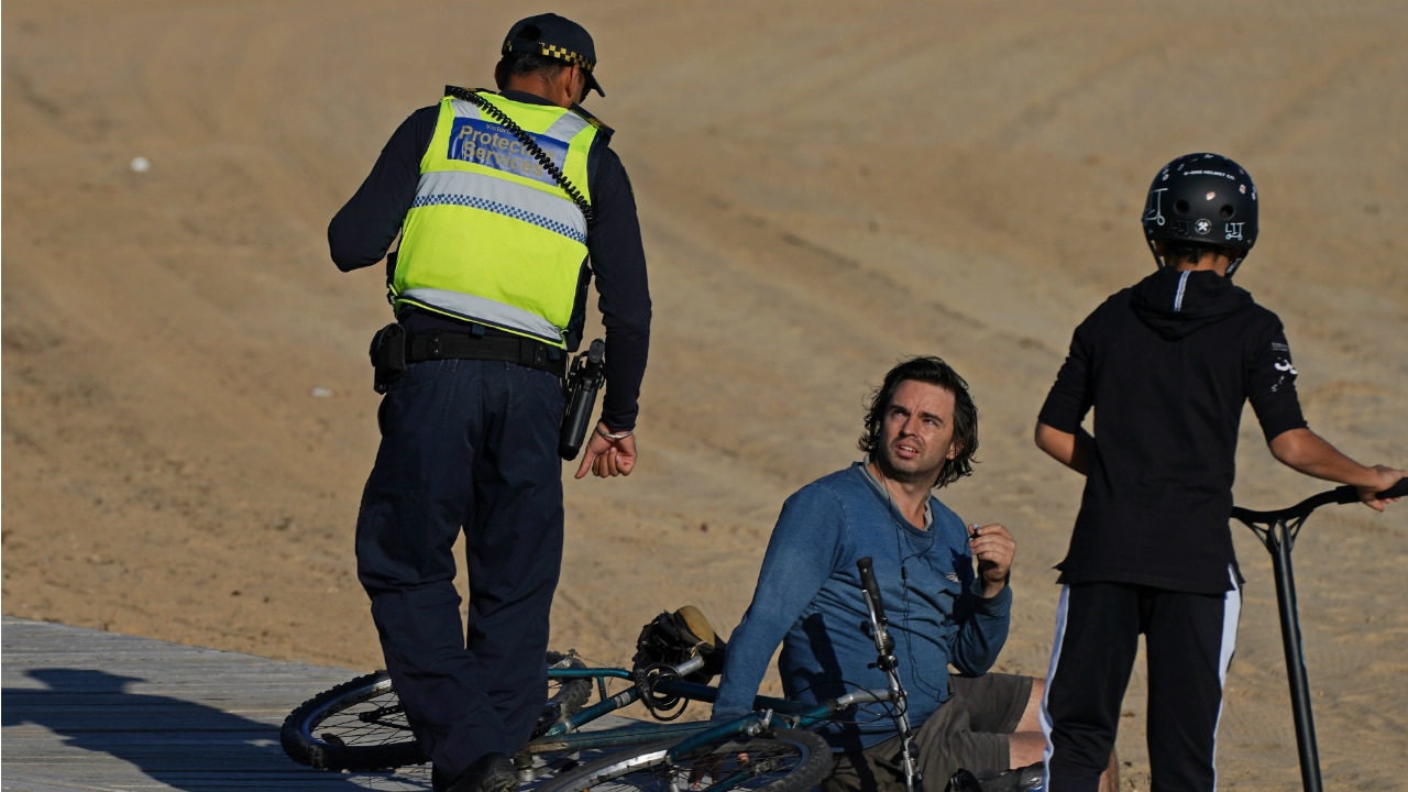 Victoria Police Protective Services Officers speak to a man at St Kilda beach. 