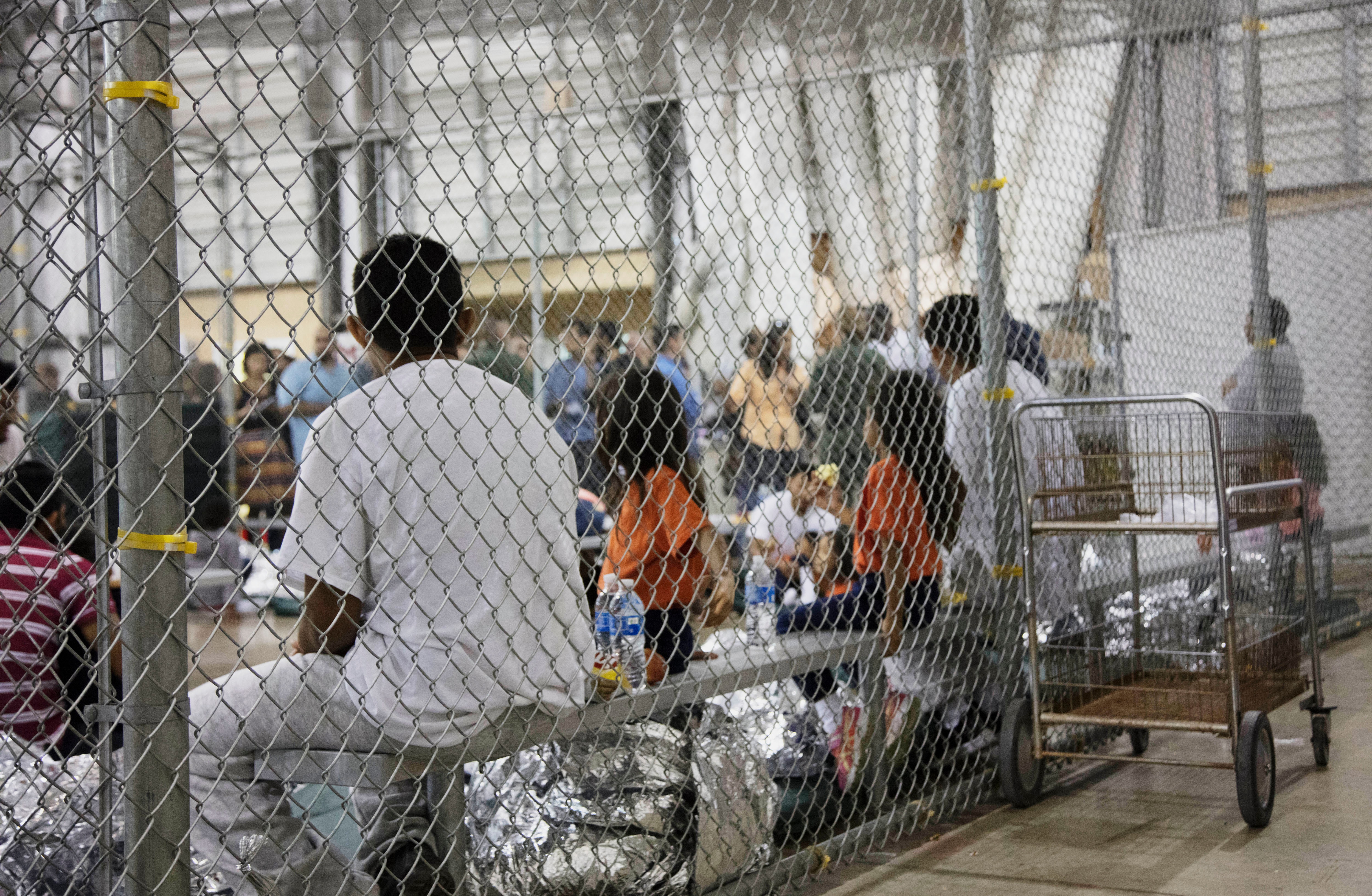 People taken into custody related to cases of illegal entry into the United States sit in cages.