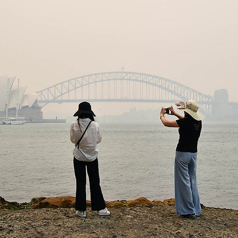 Tourists snap a photo of a smoke-filled Sydney Harbour. Tourists are staying away due to the bushfires. 