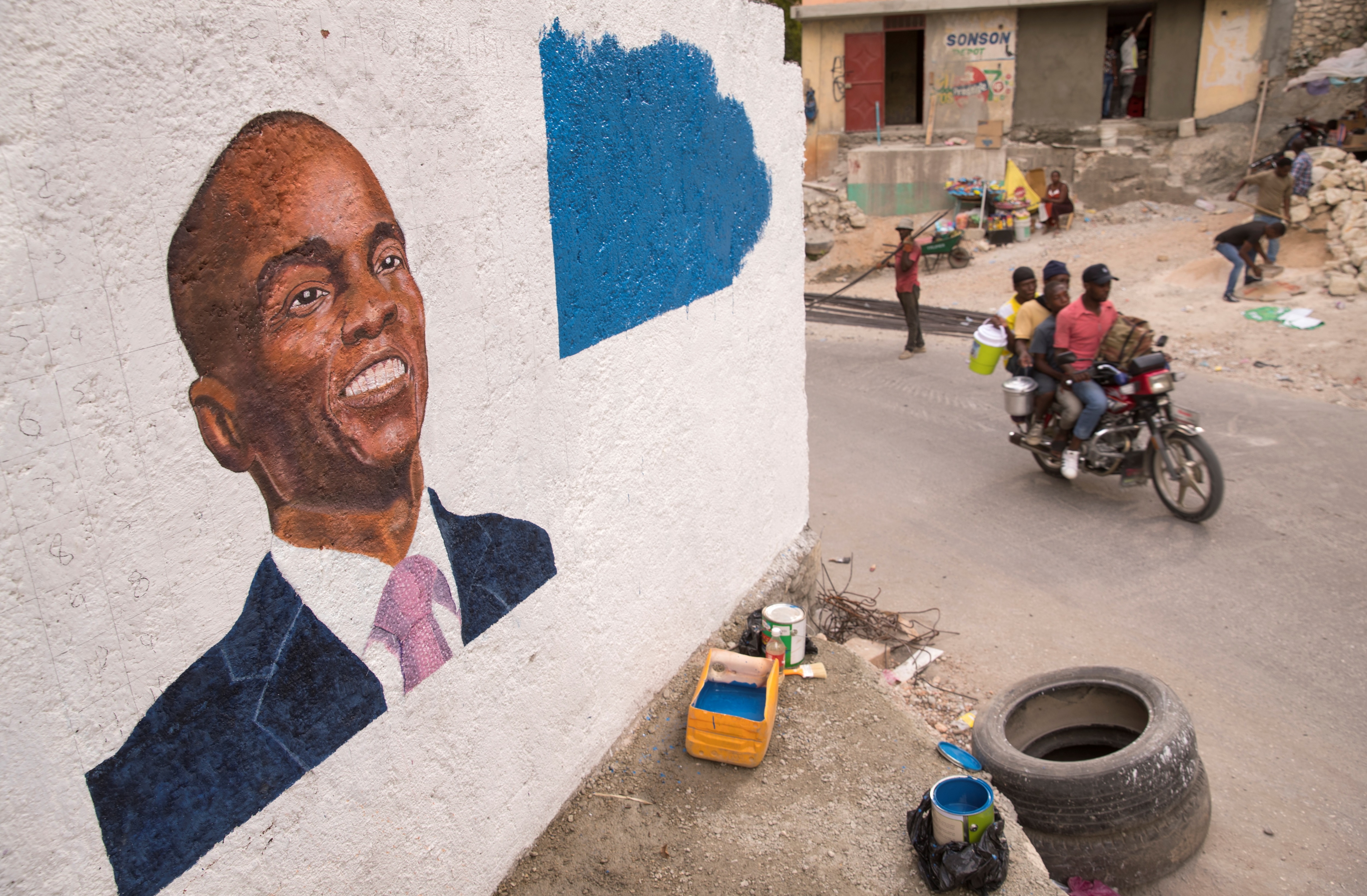 People pass by a mural in tribute to the assassinated President Jovenel Moise, in Port-au-Prince, Haiti.