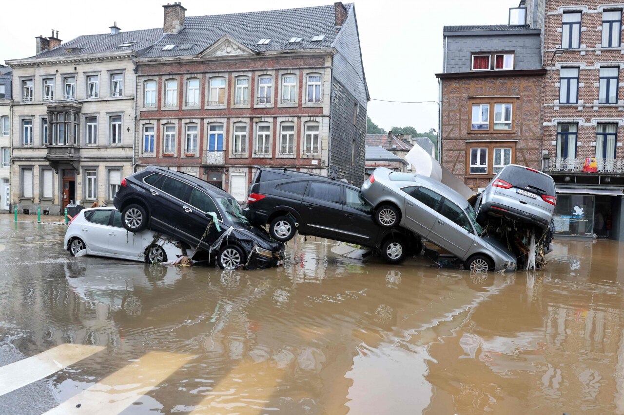Belgians pass cars piled up at a roundabout in the city after heavy rains and floods lashed western Europe