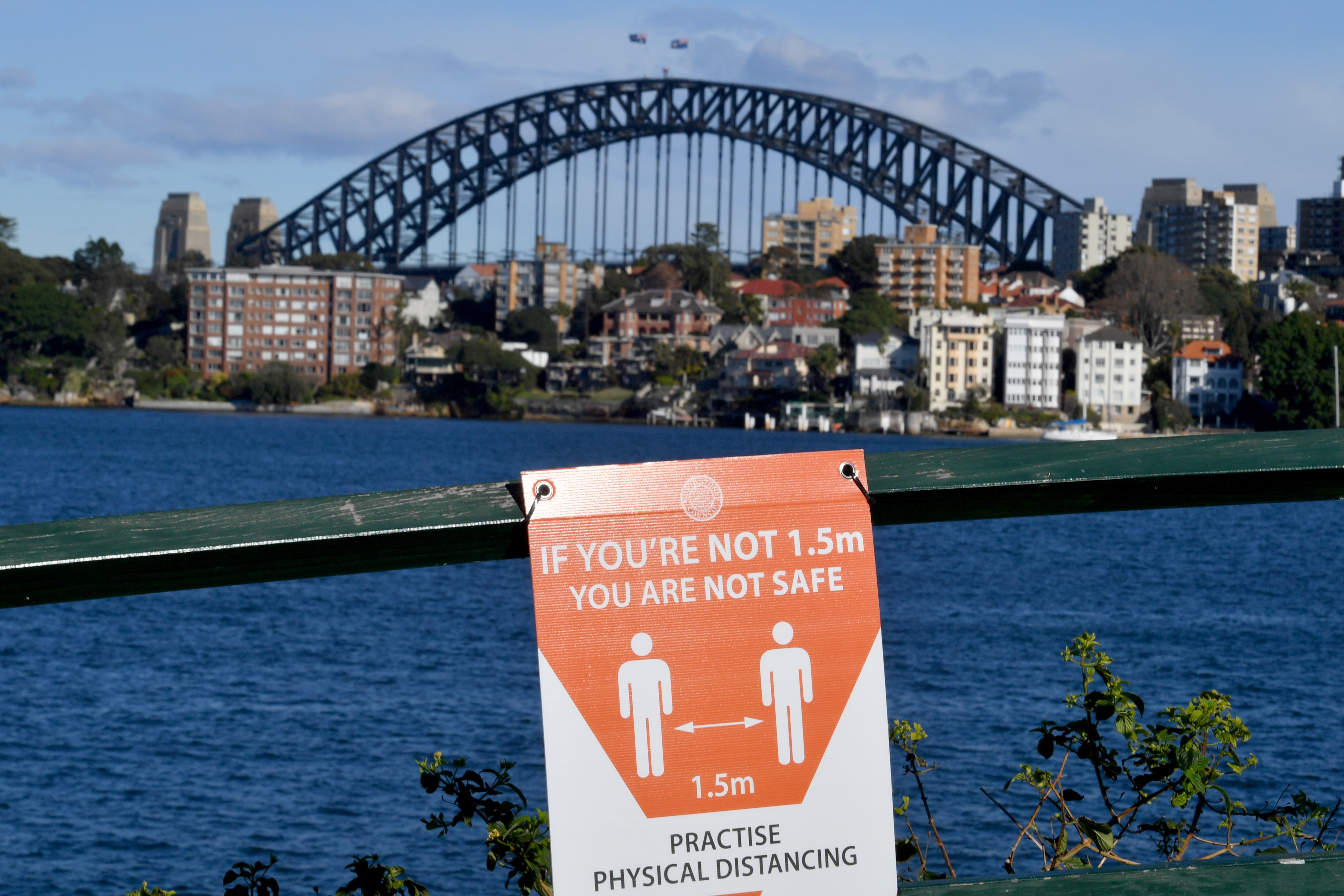 A sign warning people to socially distance is seen on the foreshore in front of the Sydney Harbour Bridge on Friday, 16 July, 2021. 