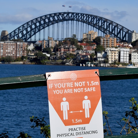 A sign warning people to socially distance is seen on the foreshore in front of the Sydney Harbour Bridge on Friday, 16 July, 2021. 