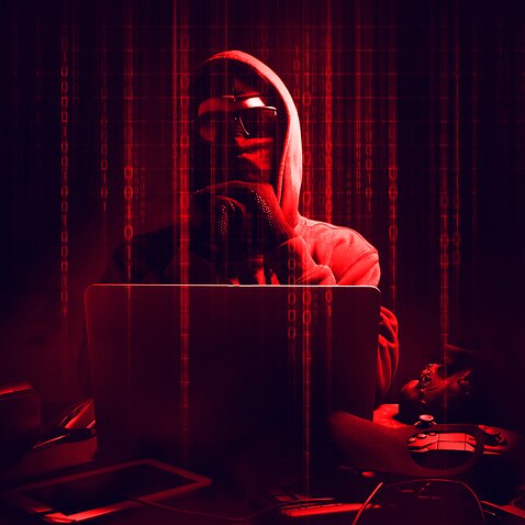 Digital Composite Image Of Male Hacker Using Laptop With Binary Codes In Darkroom