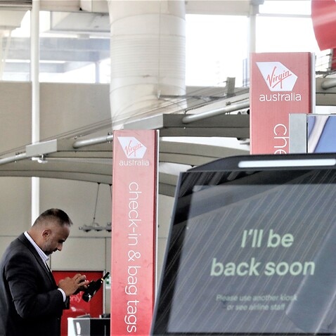 A Virgin Australia worker uses his phone at the check-in counters at Sydney Airport in Sydney, Wednesday, April 22, 2020. 