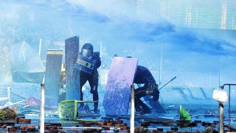 Hong Kong'da protestocular kalkanların arkasında gizleniyor. Protestors duck behind shields as a blue-dyed liquid is sprayed from an armored police vehicle at the Hong Kong Polytechnic University.