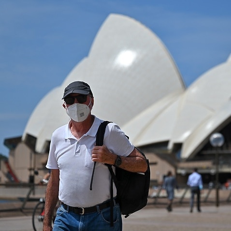 People wearing masks walk in front of the Sydney Opera House.