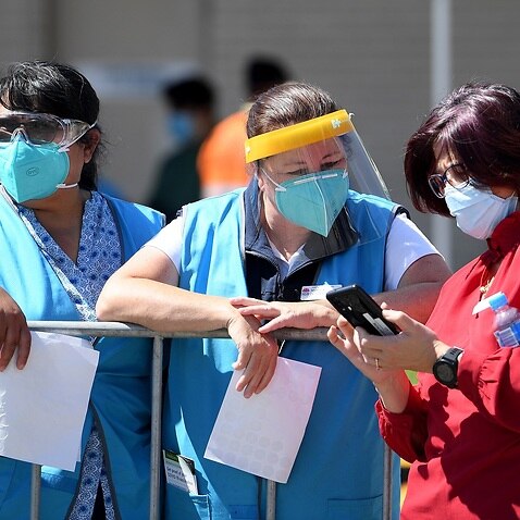 Health workers look on as NSW Premier Gladys Berejiklian addresses media during a press conference outside the Covid Vaccination hub at Macquarie Fields, south west of Sydney, Friday, September 24, 2021. (AAP Image/Dan Himbrechts) NO ARCHIVING