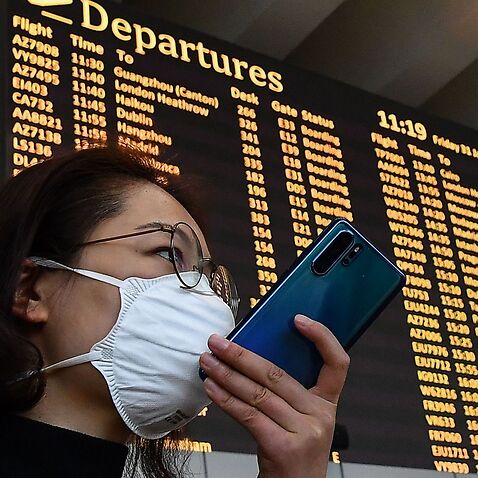 A passenger wearing a respiratory mask speaks on her smartphone by the departures board on January 31, 2020 at Rome's Fiumicino airport, as a number of airlines