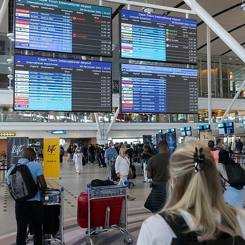 Travellers look at a flight information notice board at Cape Town International Airport as restrictions on international flights take effect 28 Nov 2021