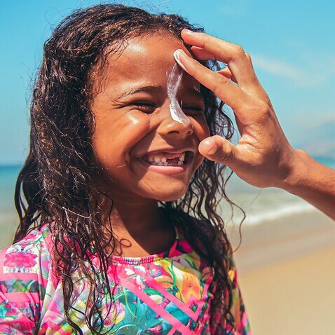 Little surfer girl preparing for surf with suntan lotion on a face