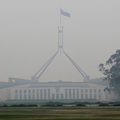 The Australian flag flies above Parliament House as smoke shrouds the capital.