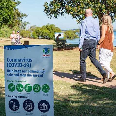 A couple walks past a sign informing population about coronavirus.
