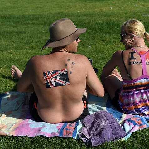 A couple with Australian flag stickers on their backs sit on the grass near Bondi Beach on Australia Day