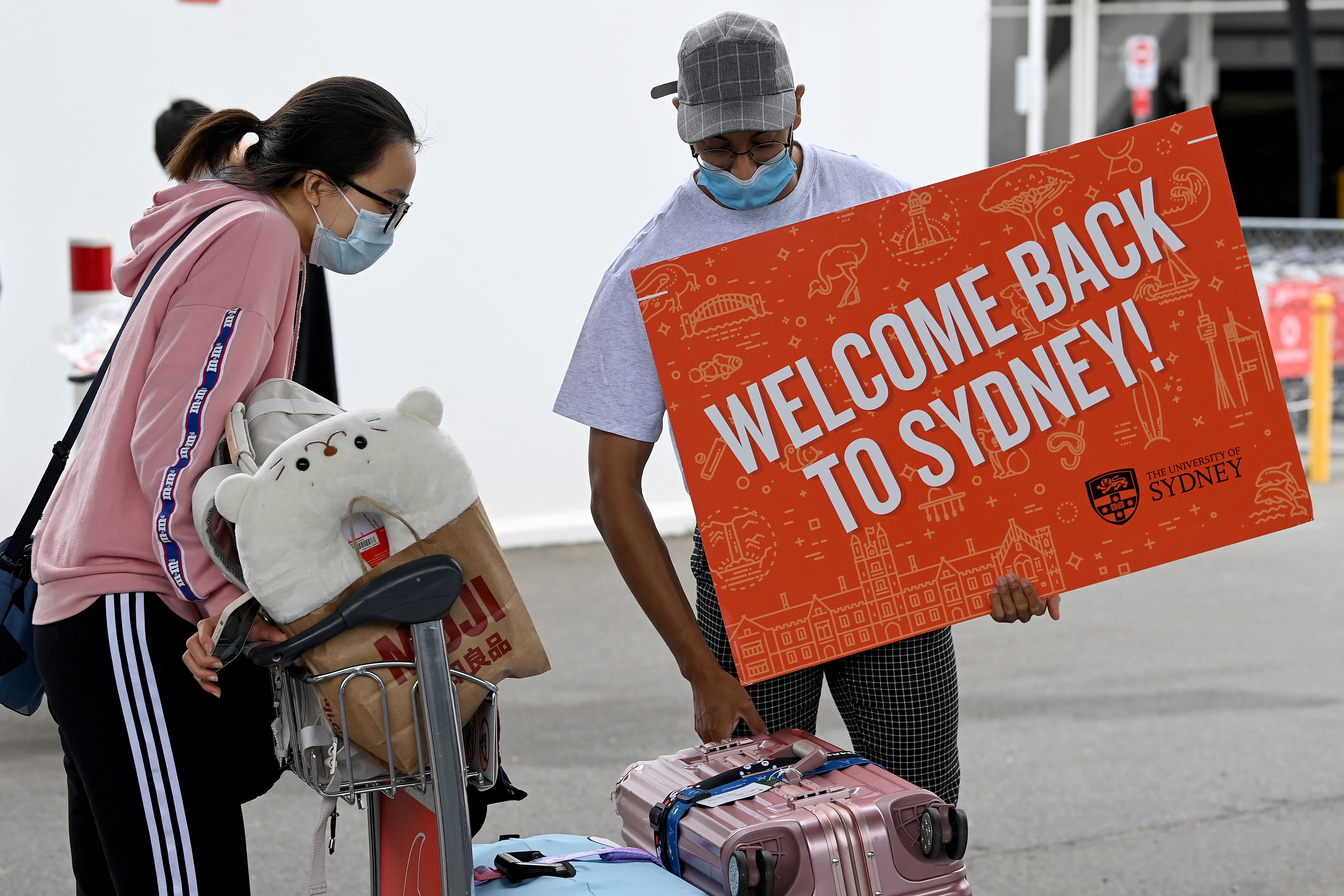 University representatives hold signs as international students arrive at Sydney Airport in Sydney