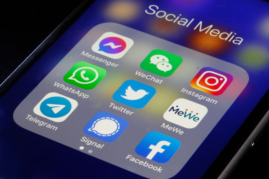 The logos of social media applications, Messenger, WeChat, Instagram, WhatsApp, Twitter, MeWe, Telegram, Signal and Facebook are displayed on an iPhone.