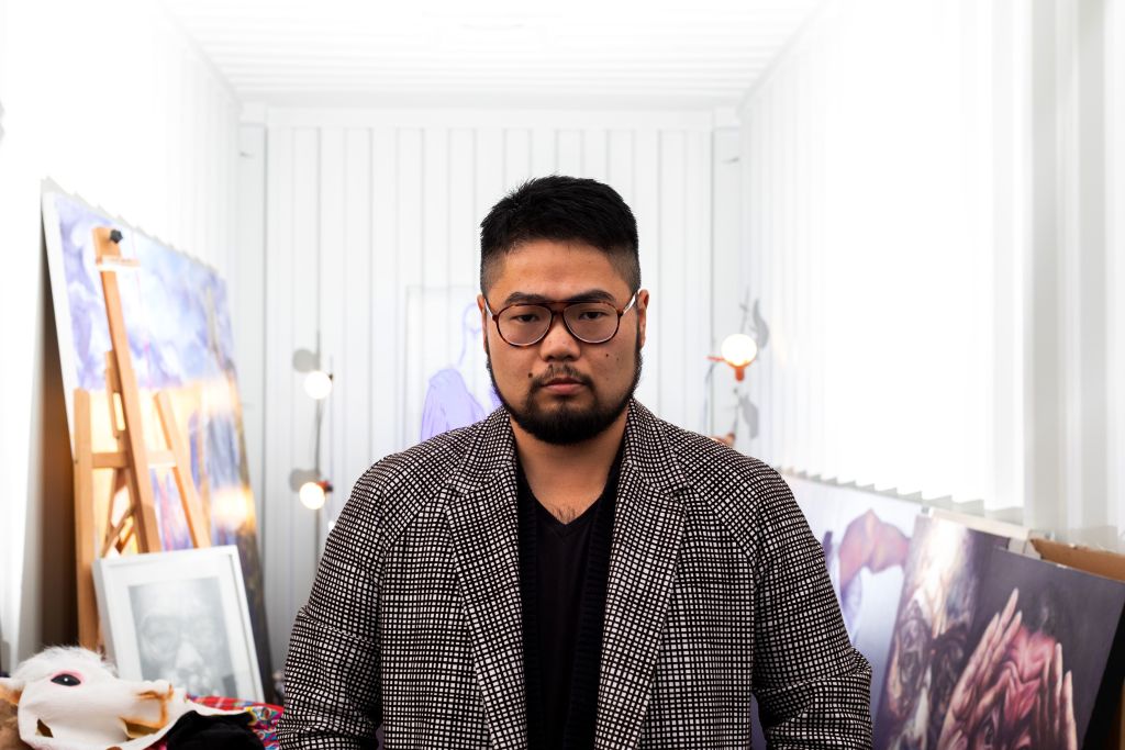 Chinese cartoonist Badiucao standing behind his artwork titled 'Light' in his studio in Melbourne.