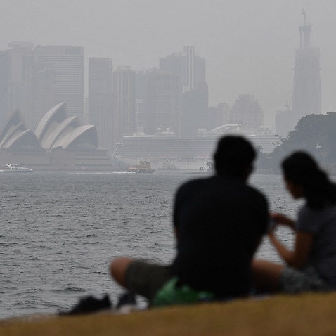 The Sydney Opera House is obscured by smoke haze from bushfires as a couple have a picnic in Sydney, Wednesday, January 8, 2020. (AAP Image/Steven Saphore) NO ARCHIVING