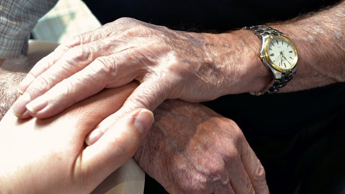 Two elderly hands holding onto a younger hand