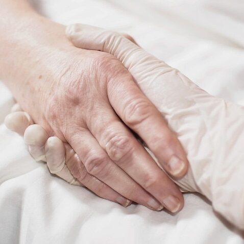 Image of a health worker's hand wearing a glove holding a patient's hand