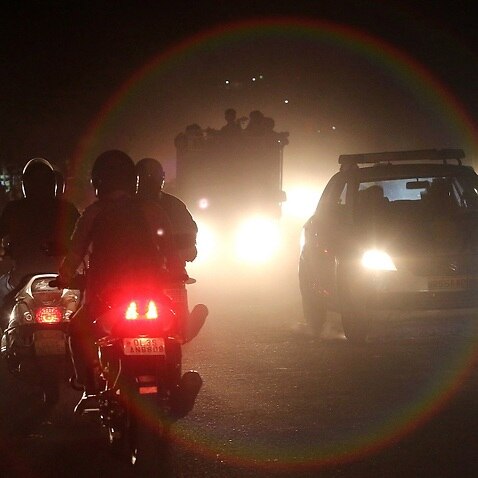 Indian people commute on motorcycles and cars through heavy dust and smog in New Delhi.