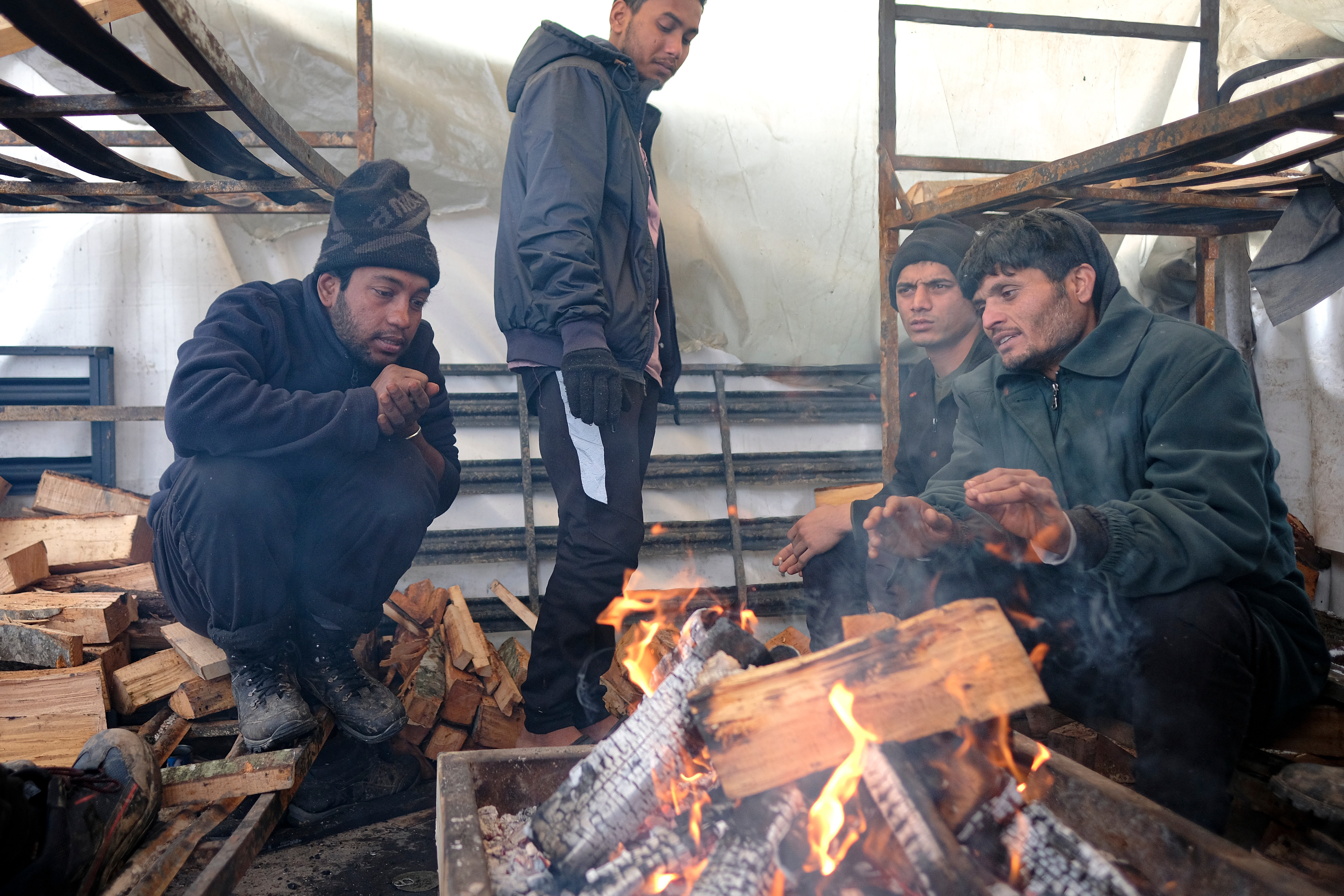 Migrants warm themselves around a fire in a makeshift tent at the Lipa camp, outside Bihac, Bosnia