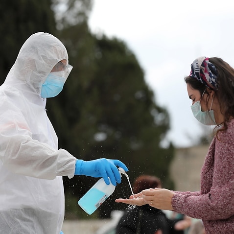 A worker wearing a protective suit pours disinfectant on the hands of a voter at a special voting station for people in coronavirus quarantine, in Jerusalem.