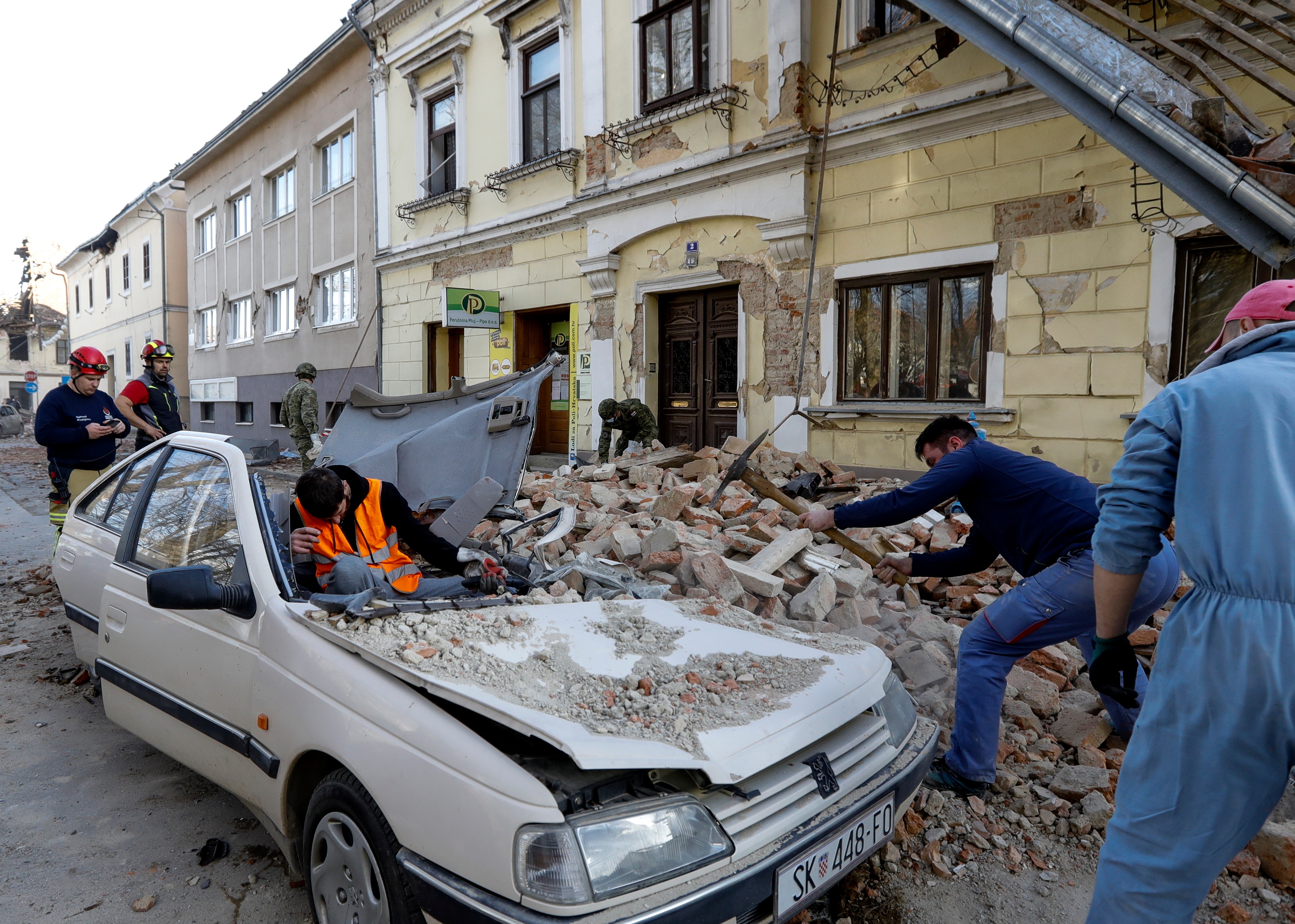 Personas y soldados limpian los escombros junto a automóviles y edificios que resultaron dañados por un terremoto en Petrinja, Croacia. 