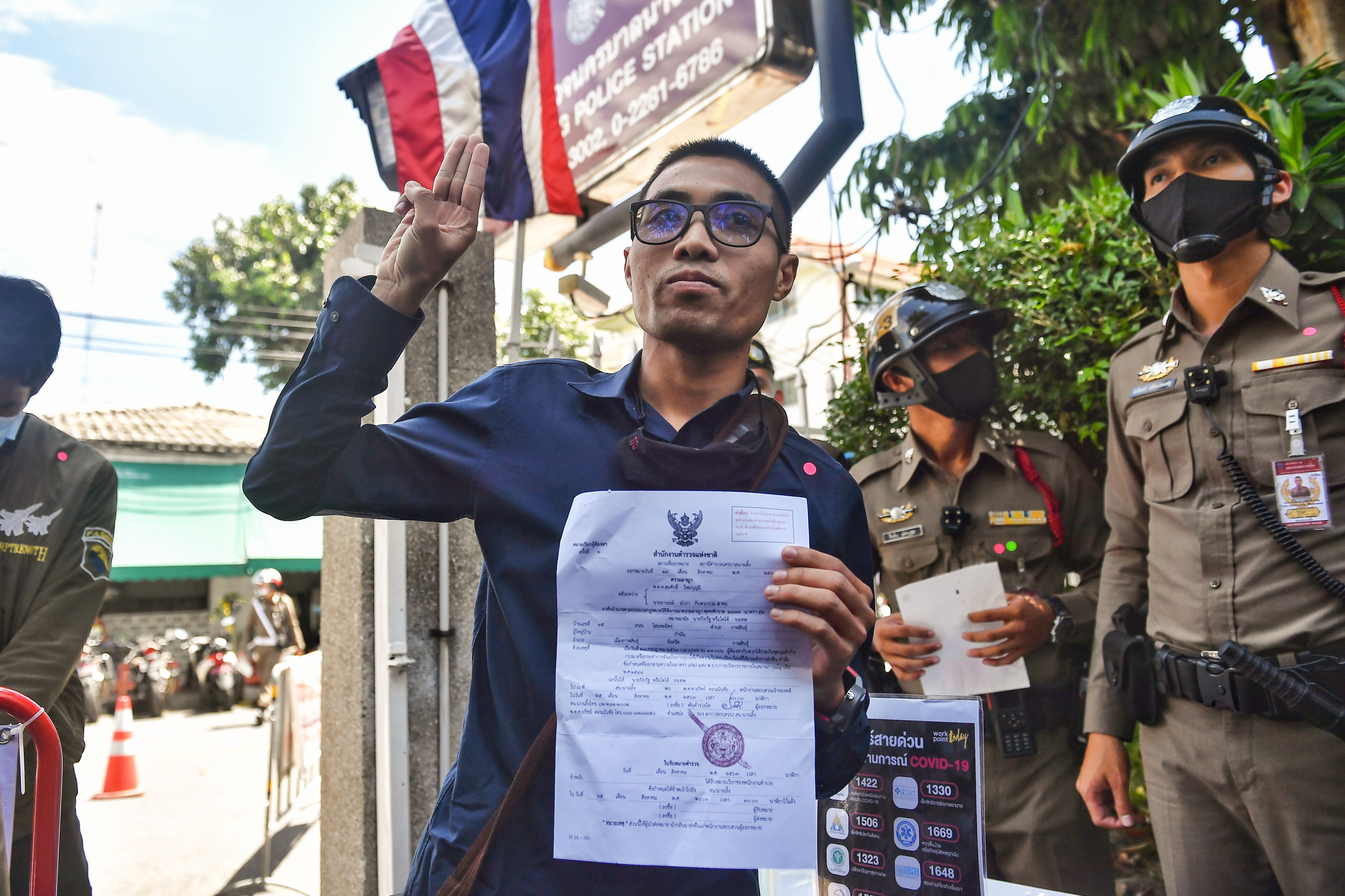 Activist Piyarat Chongthep gives the three-fingered Hunger Games salute as he arrives at a Bangkok police station to accept charges relating to a protest.