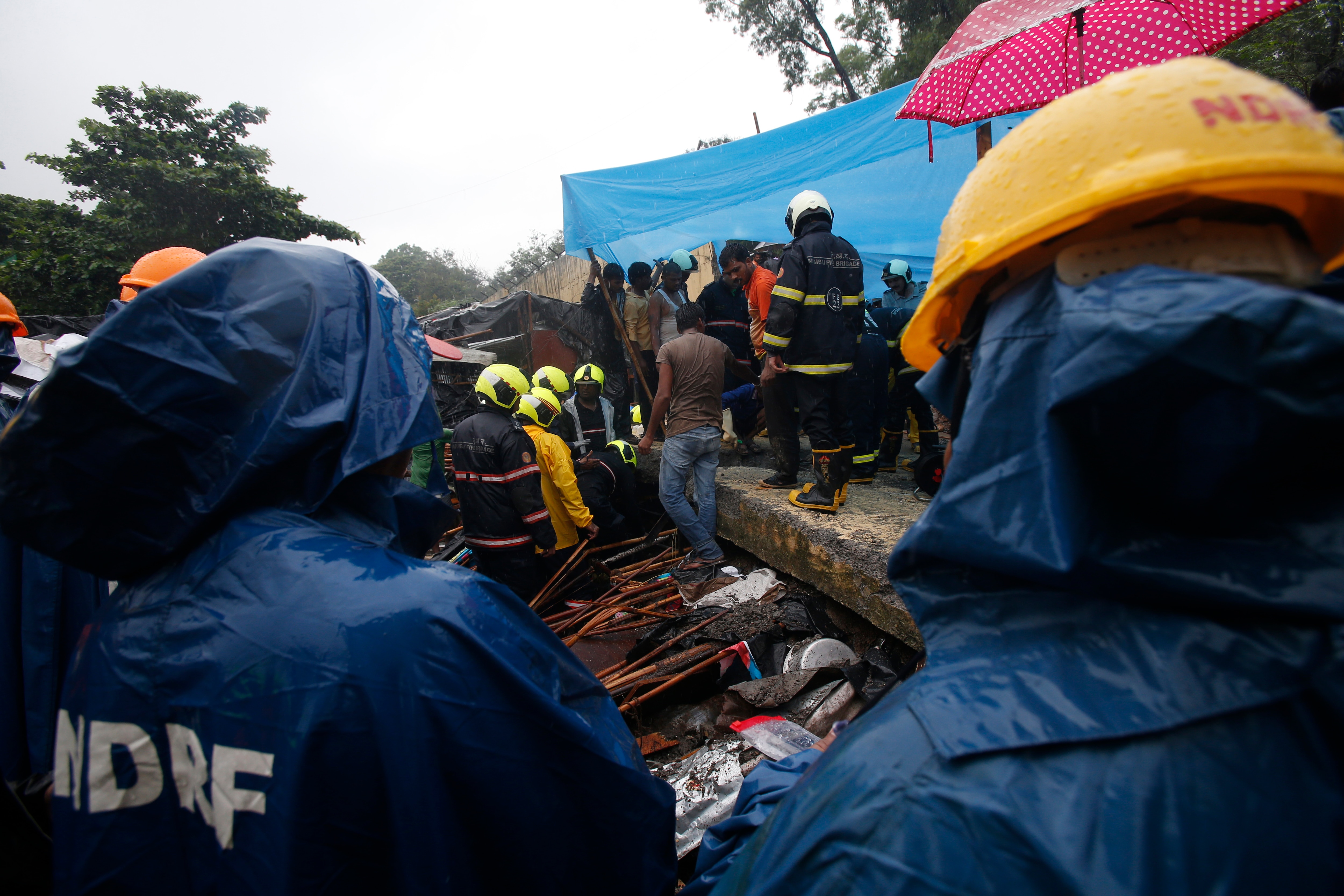 Rescuers of the National Disaster Response Force stand at the spot after heavy rainfall caused a wall to collapse onto shanties, in Mumbai, India.