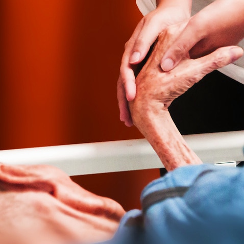 Image of an elderly person's hand being held by younger persons's hands.