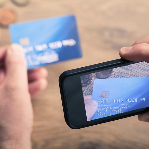 A person takes a photo of their credit card on their mobile phone to send to a scammer. 