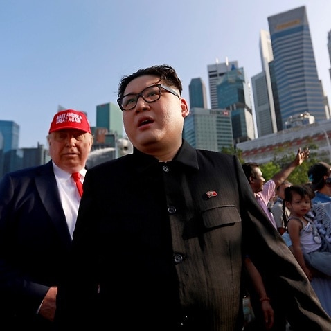 Kim Jong-un impersonator Howard X (C) and Donald Trump impersonator Dennis Alan (L) walk together at the Merlion Park in Singapore in 2018.