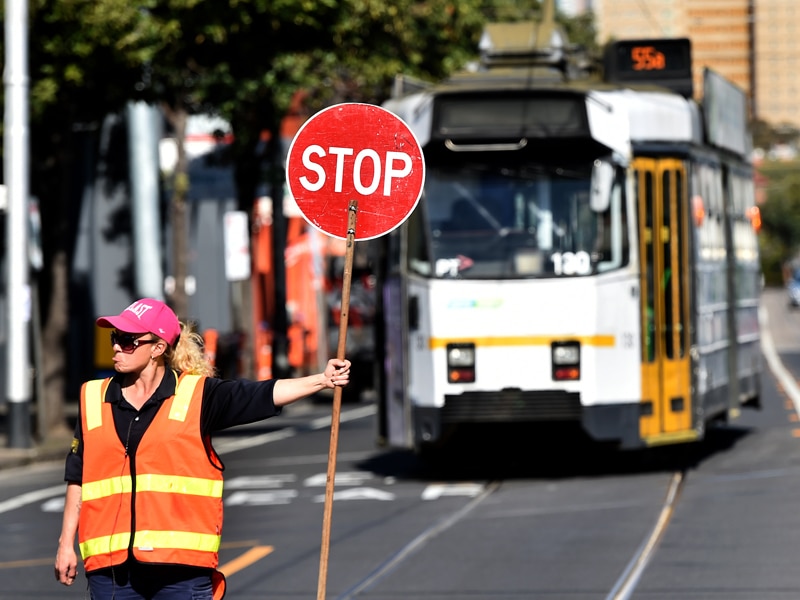 A traffic controller holds a stop signs as a tram rejoins the network