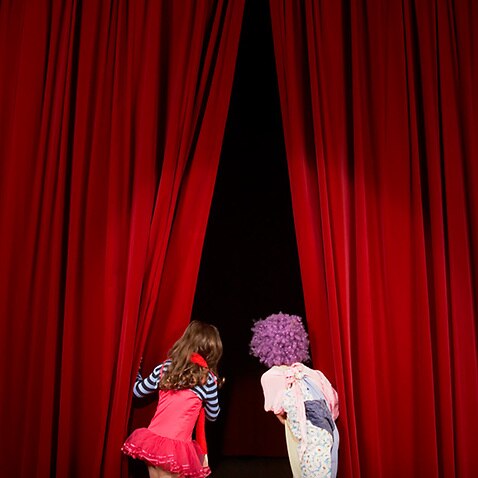 Children on theatre stage, looking through red curtains
