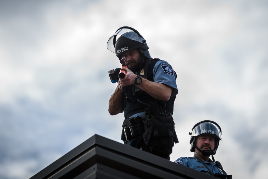 Two police officers stand on the roof of the Third Police Precinct holding a projectile launcher during a demonstration in a call for justice for George Floyd
