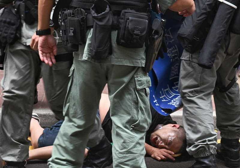 Hong Kong police officers detain a protester after he was pepper sprayed during the rally on 1 July, 2020 Hong Kong police officers detain a protester after he was pepper sprayed on 1 July, 2020
