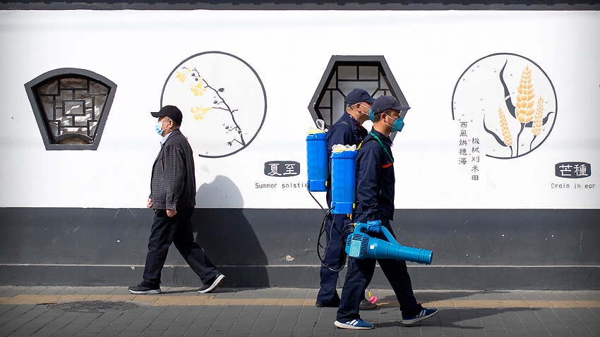 Workers wearing face masks and carrying disinfectant sprayers walk along a street in Beijing.