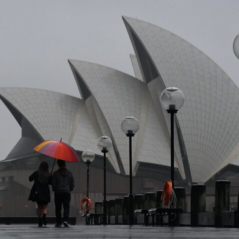 Pedestrians walk past the Sydney Opera House during wet weather in Sydney, Wednesday, November 10, 2021