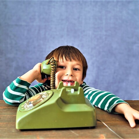A kid talking via an old-fashioned phone. 