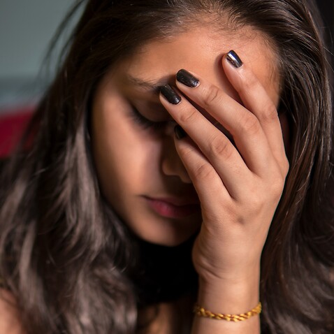 ndoor image of sad, depressed young girl feeling headache and thinking by holding her head and looking down at home.