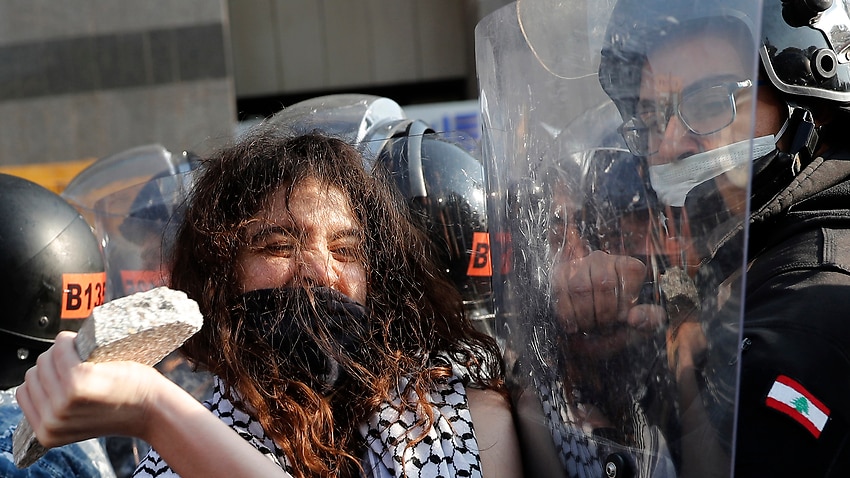 An anti-government protester confronts police with a stone during a protest against the deepening financial crisis in Lebanon.
