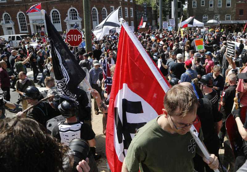 A white supremacist carrying a Nazi flag into the entrance to Emancipation Park in Charlottesville, 2017. This Saturday, Aug. 12, 2017 image shows s white supremacist carrying a NAZI flag into the entrance to Emancipation Park in Charlottesville, Va.